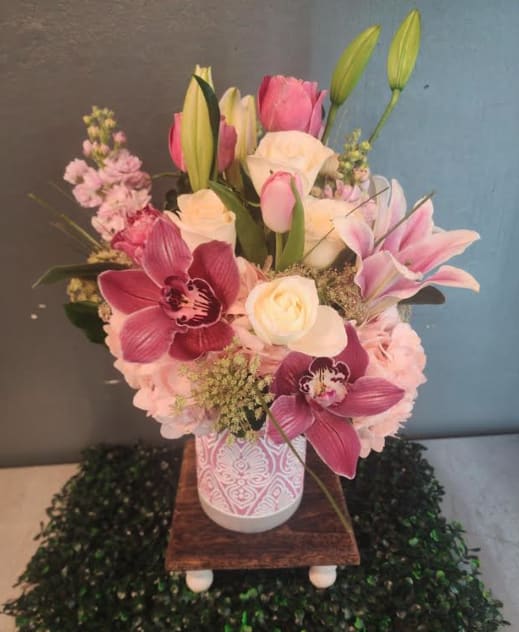 Pink and white mixed flower arrangement with orchids, roses, lilies, and tulips in a patterned vase.