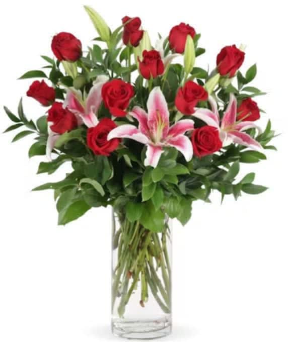 Tall clear vase with red roses and pink lilies arranged in a lush, upright bouquet