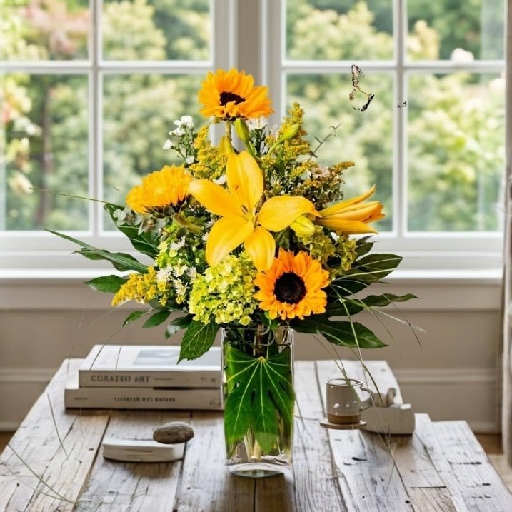 Taking Flight - Lift their spirits high. Taking Flight's sunny yellows will have them soaring with happiness. Yellow lilies, sunflowers and other flowers are playfully arranged in this sunny arrangement.