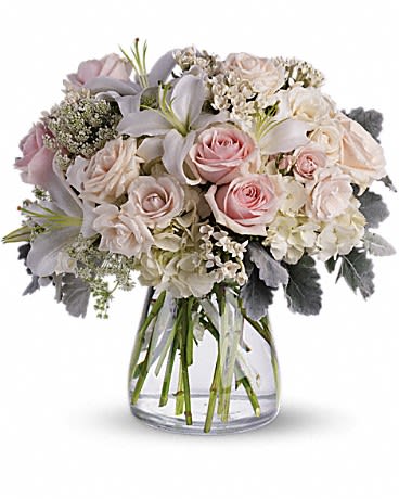 Round arrangement of white lilies, pale pink roses, and cream blooms in a clear glass vase