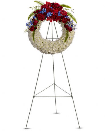 Standing wreath of white flowers with red roses and blue blooms on a metal easel