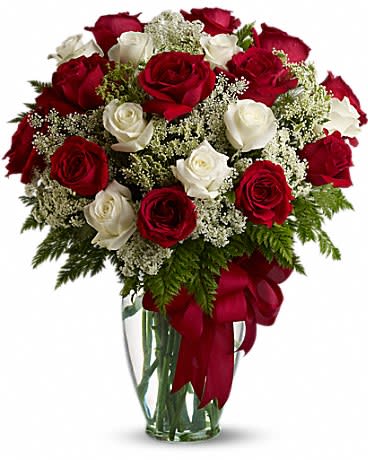 Arrangement of red and white roses with white filler flowers in a clear glass vase with a red bow