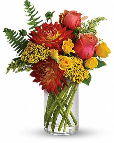 Warm arrangement of red dahlias and yellow and pink roses in a clear glass cylinder vase