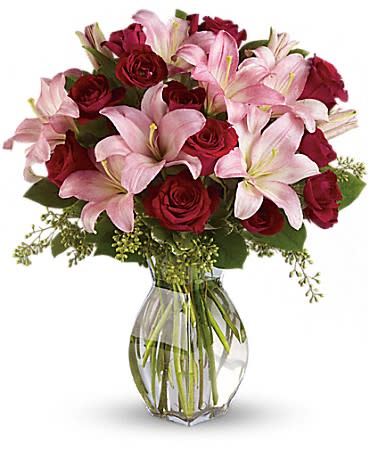 Clear glass vase filled with pink lilies and red roses in a rounded bouquet