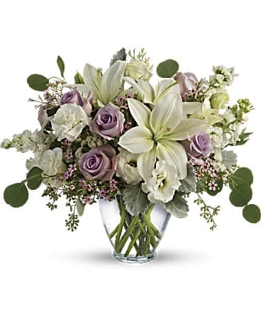 Arrangement of white lilies and pale lavender roses in a clear glass vase