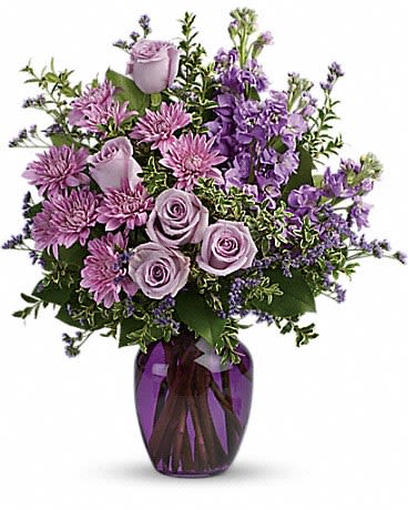 Purple and lavender roses, mums, and stock arranged in a purple glass vase.