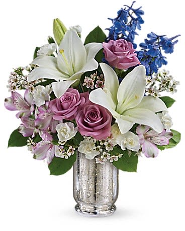 Arrangement of white lilies, lavender roses, and blue delphinium in a silver vase