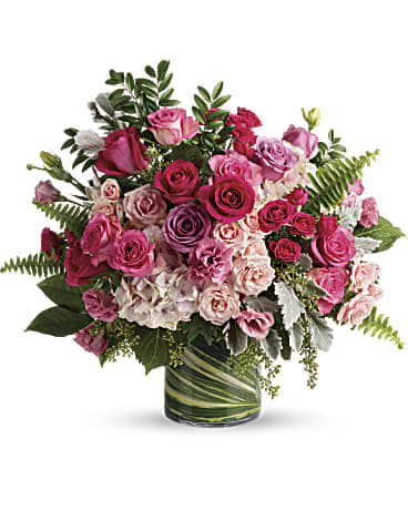Rounded arrangement of pink and lavender roses in a clear cylinder vase