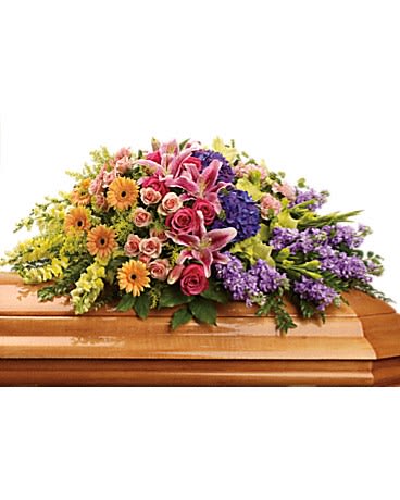 Colorful casket spray with pink lilies, roses, and mixed flowers on a wooden casket