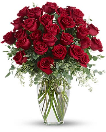 Tall arrangement of long-stemmed red roses in a clear glass vase with filler