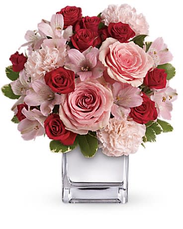 Low arrangement of pink and red roses with pale carnations in a clear glass cube vase