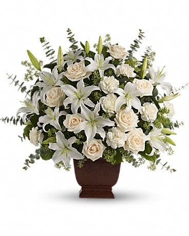 Large white lilies, cream roses, and carnations arranged in a dark pedestal vase.