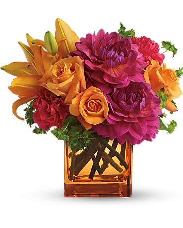 Bright arrangement of orange lilies and roses with fuchsia dahlias in an orange glass cube vase
