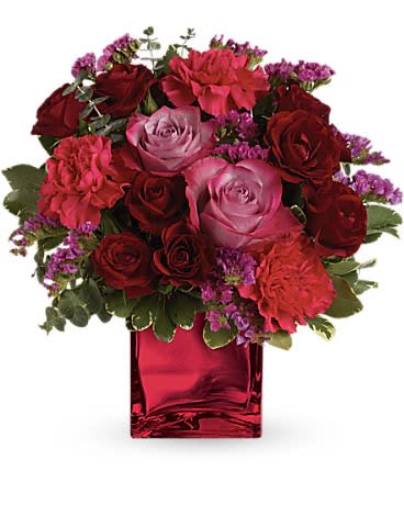 Compact bouquet of red and pink flowers in a red glass cube vase