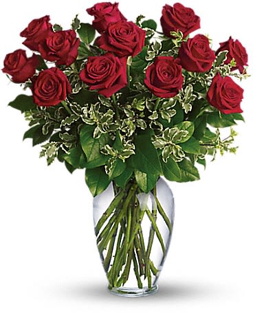 Tall arrangement of red roses in a clear glass vase with variegated foliage