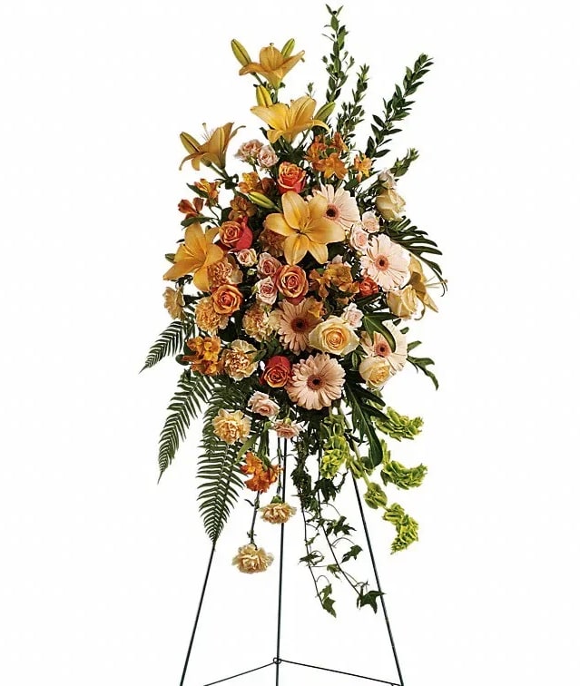 Tall standing floral spray with yellow lilies, roses, and daisies on a metal easel