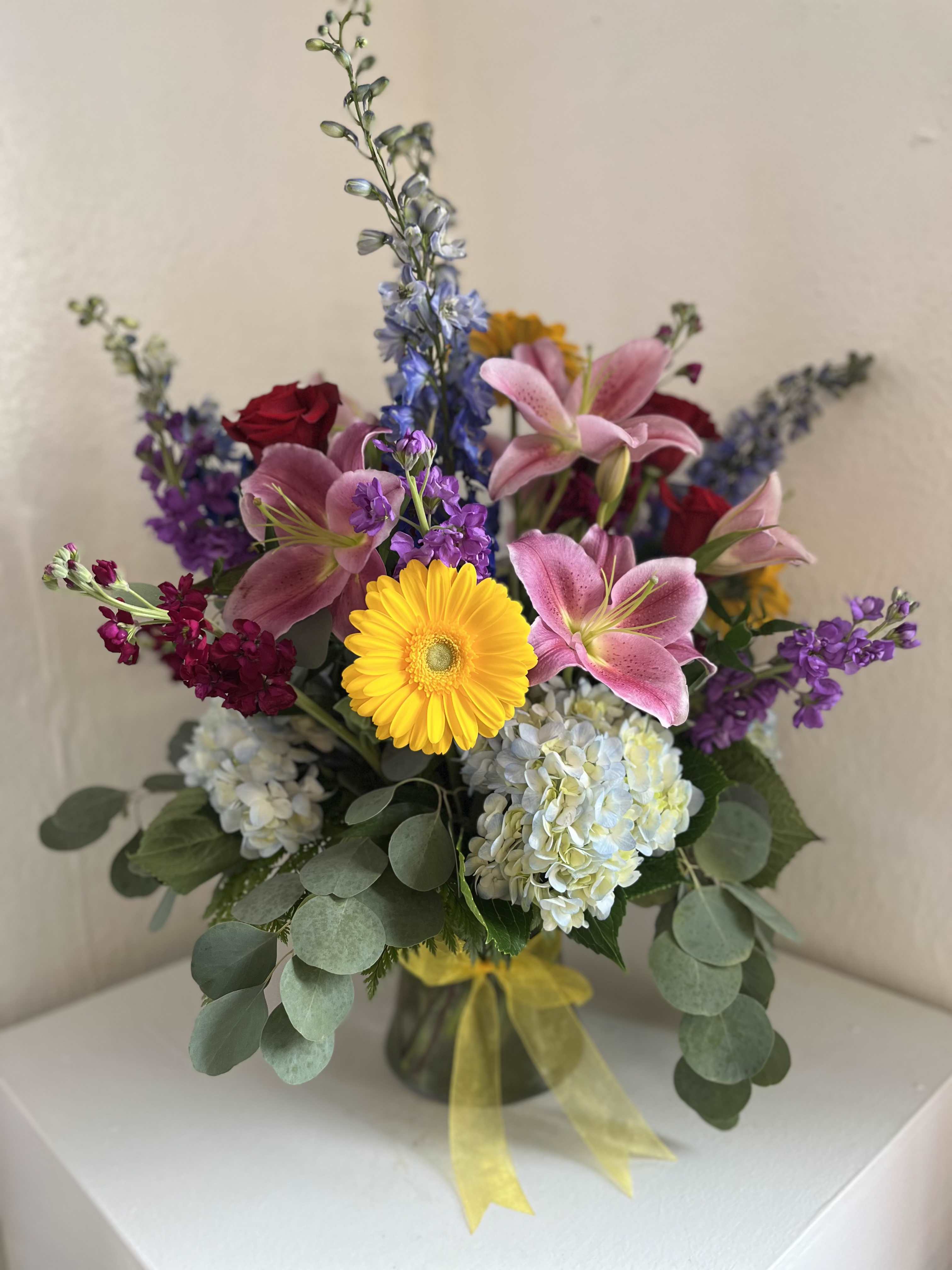 Mixed bouquet with pink lilies, yellow gerbera daisy, hydrangeas, and purple flowers in a vase