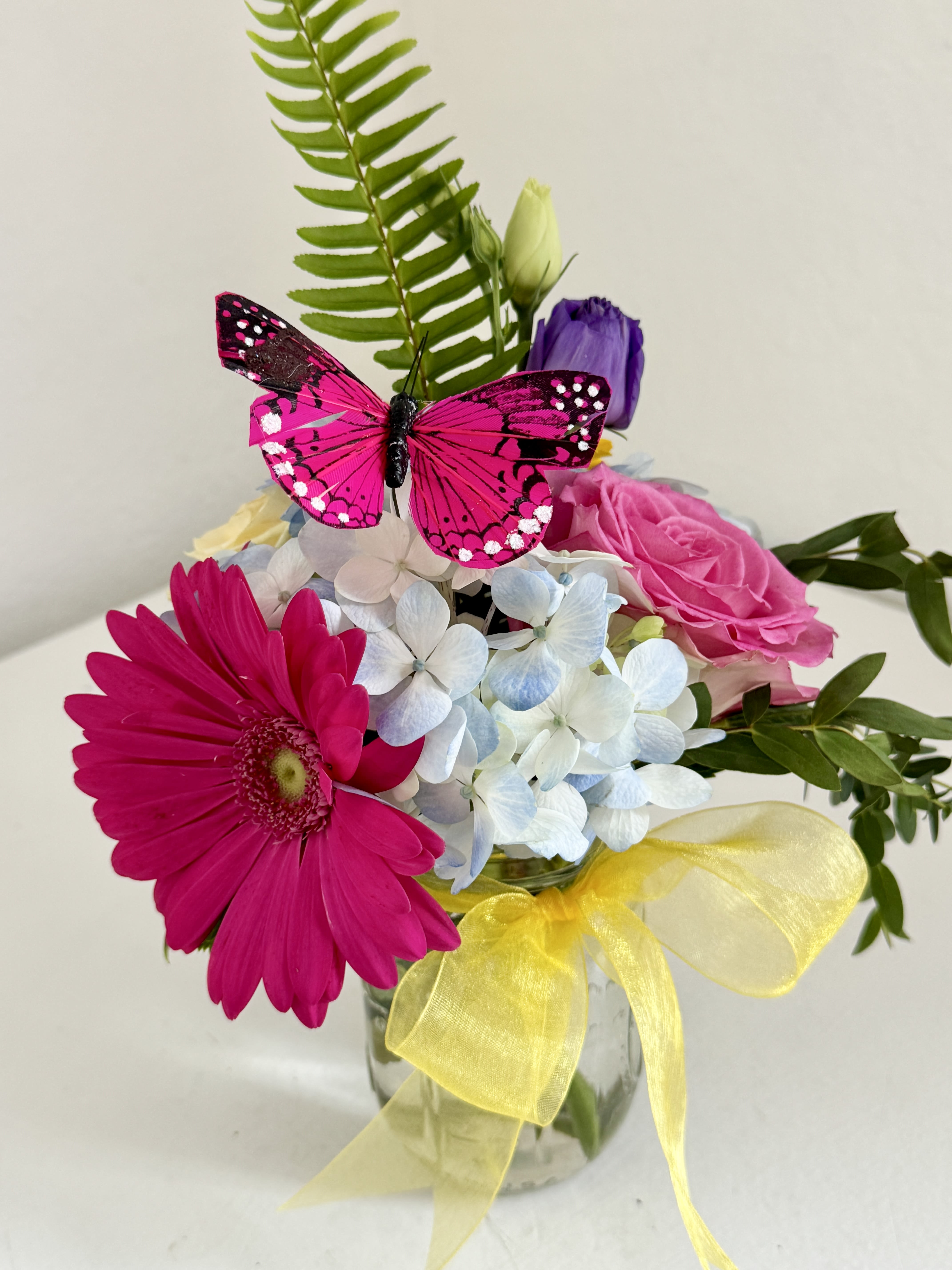 Bouquet of pink and white flowers in a glass vase with a yellow ribbon and butterfly decoration