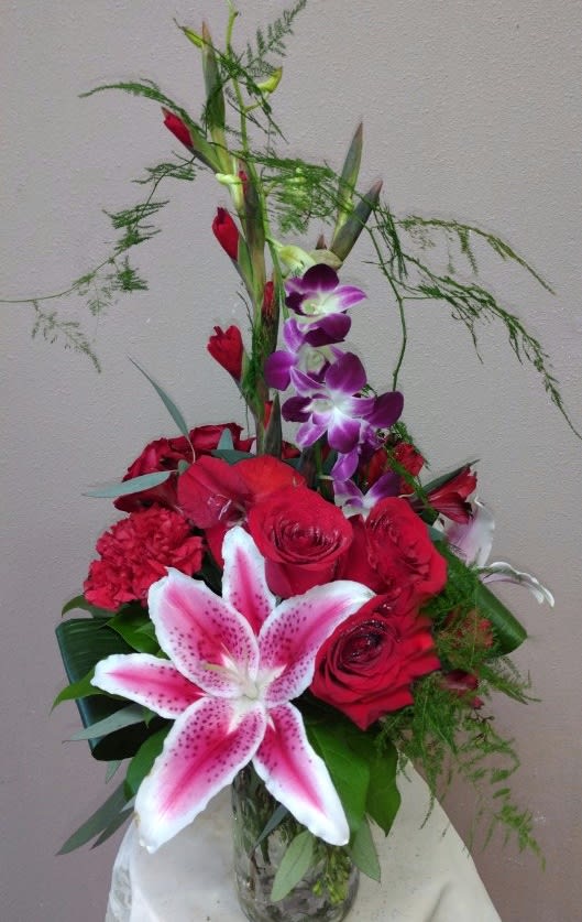 Tall bouquet of red roses, pink lily, and purple orchids in a glass vase