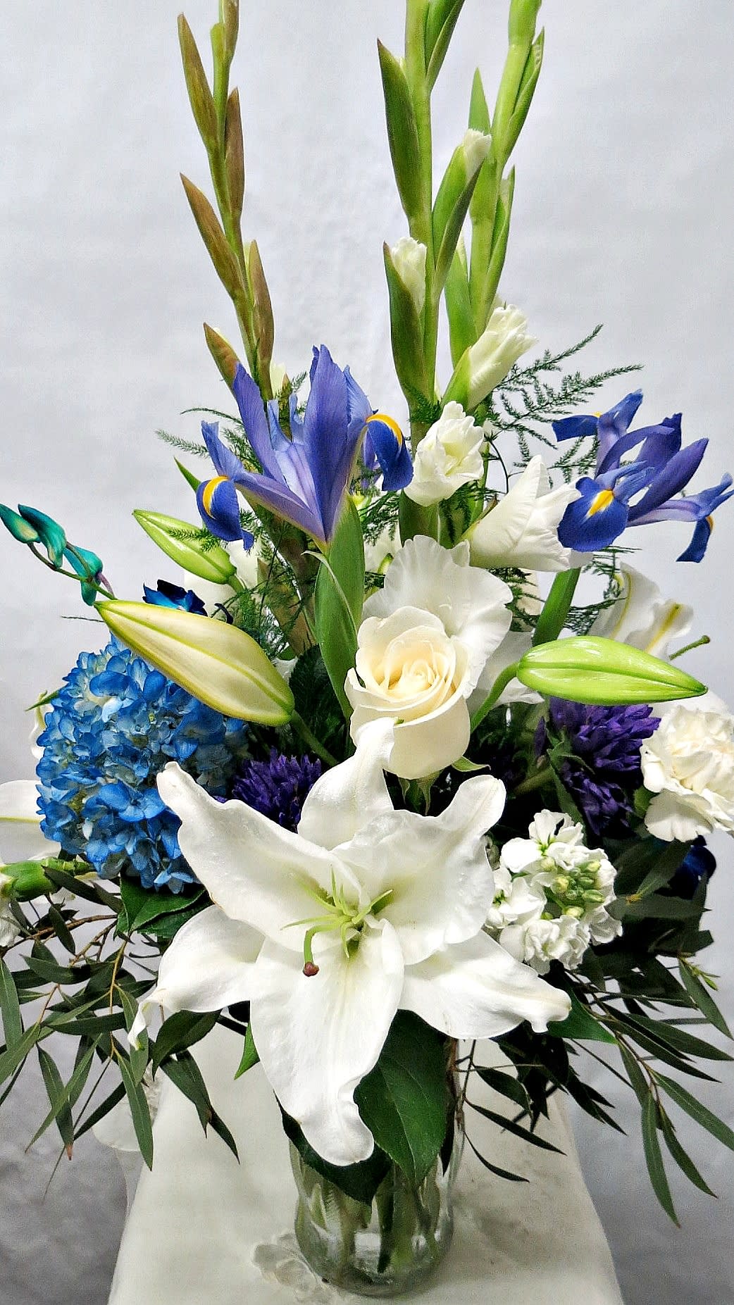 White lilies, blue irises, and a blue hydrangea arrangement in a glass vase