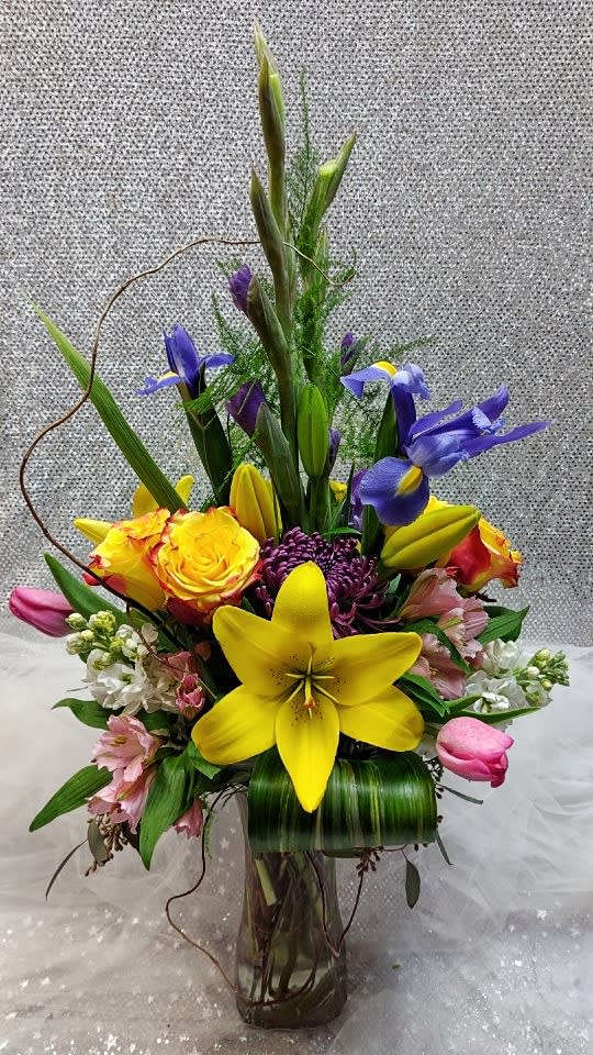 Tall mixed bouquet in a glass vase with yellow lilies and purple irises