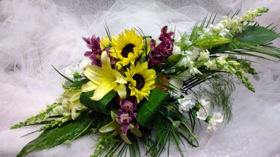 Bouquet with sunflowers, lilies, and purple orchids on white fabric