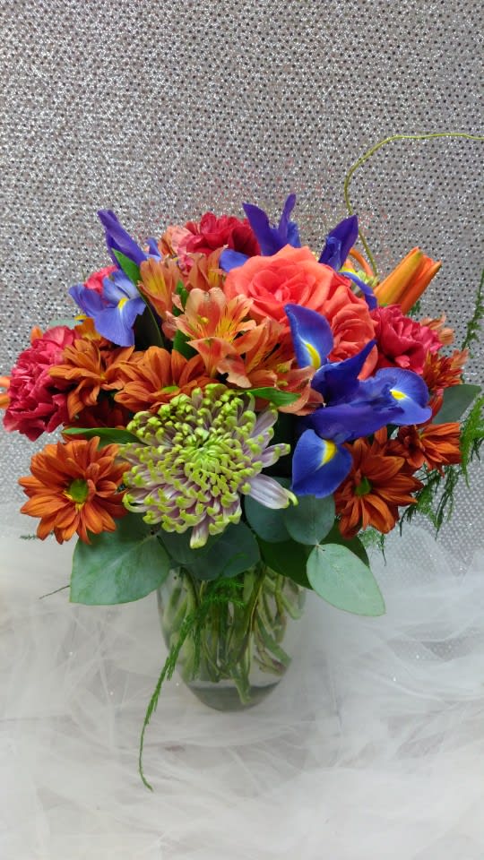 Mixed bouquet of orange, pink, and blue flowers in a glass vase
