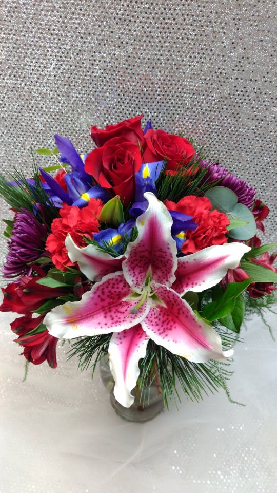 Bouquet of red roses, pink lilies, and purple flowers in a glass vase