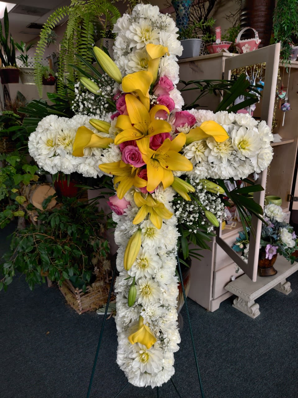 Cross-shaped floral tribute with white blooms, yellow lilies, and pink roses