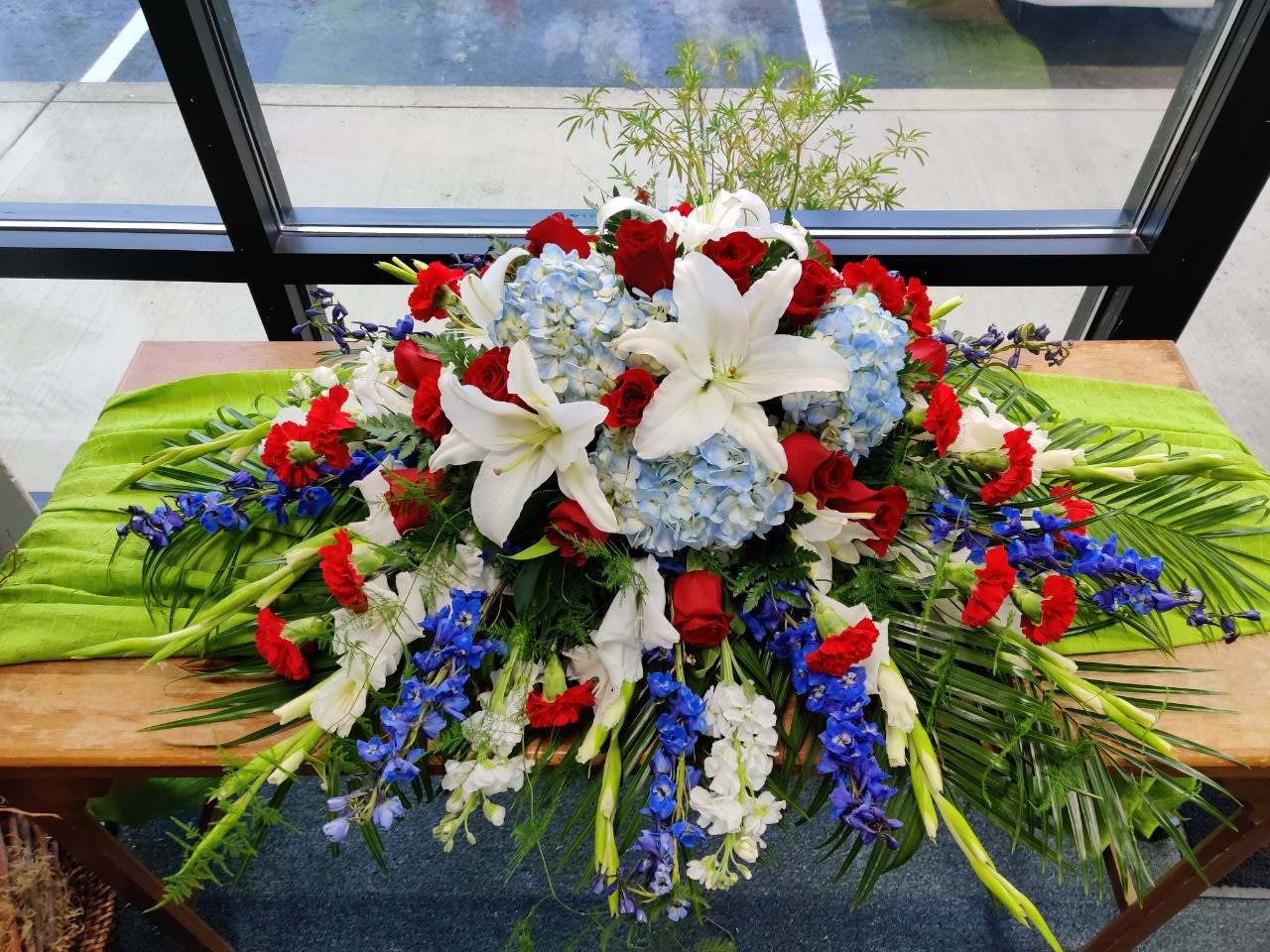 Large floral casket spray with white lilies, red roses, and blue hydrangeas