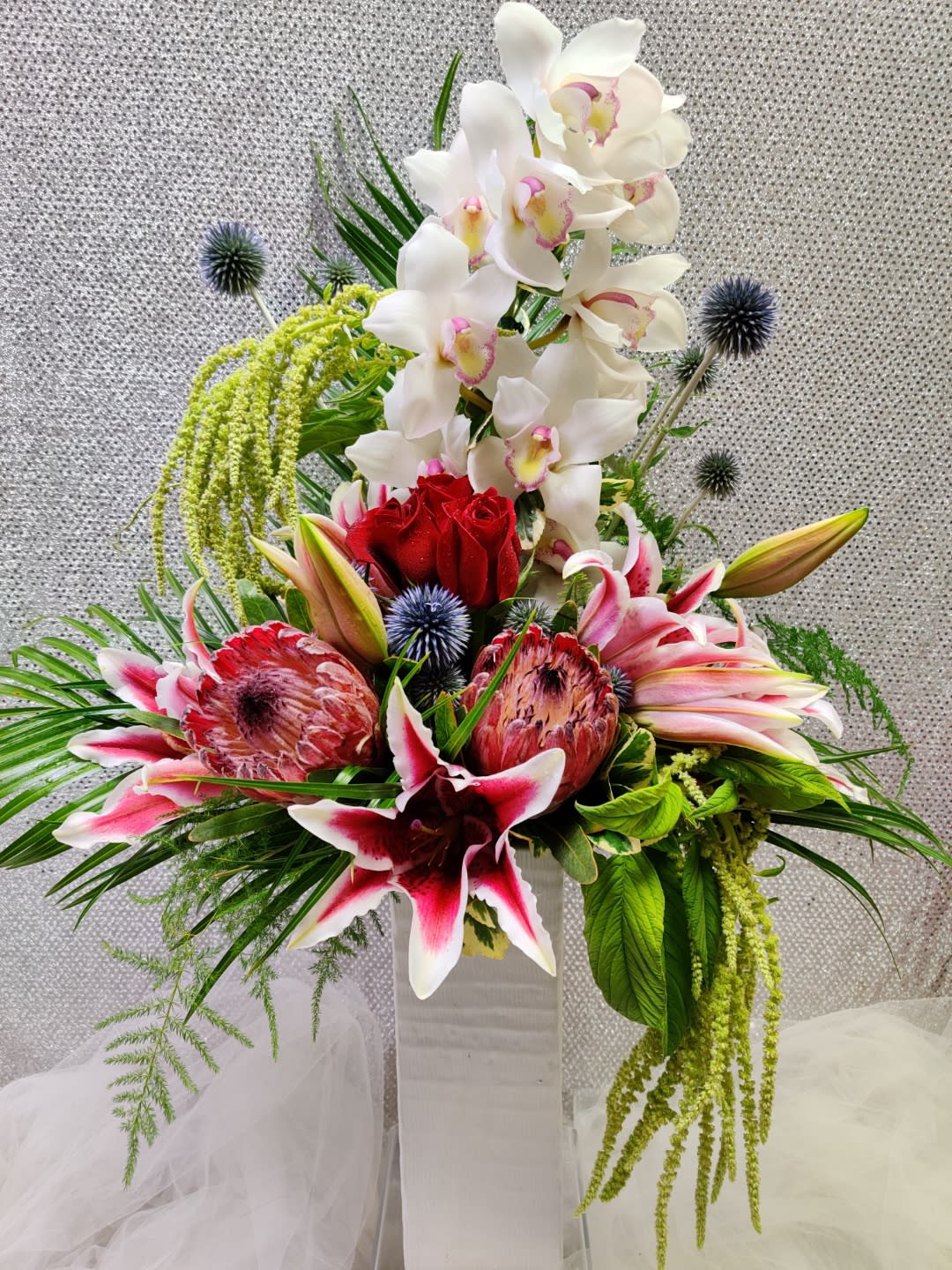 Tall floral arrangement with white orchids, red roses, and pink lilies in a white vase