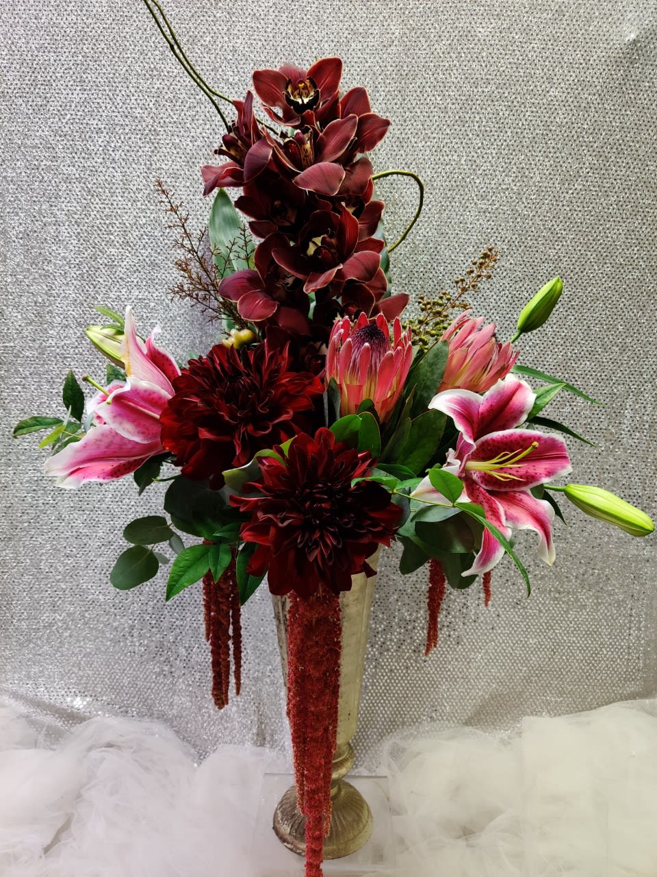 Tall floral arrangement with burgundy orchids and pink lilies in a gold vase