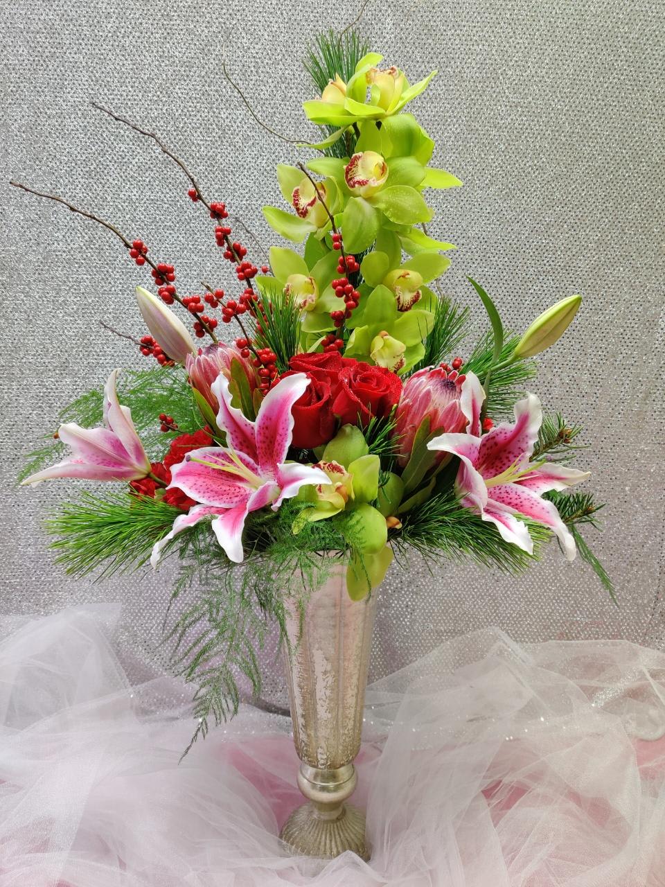 Tall floral arrangement with orchids, roses, and lilies in a gold vase