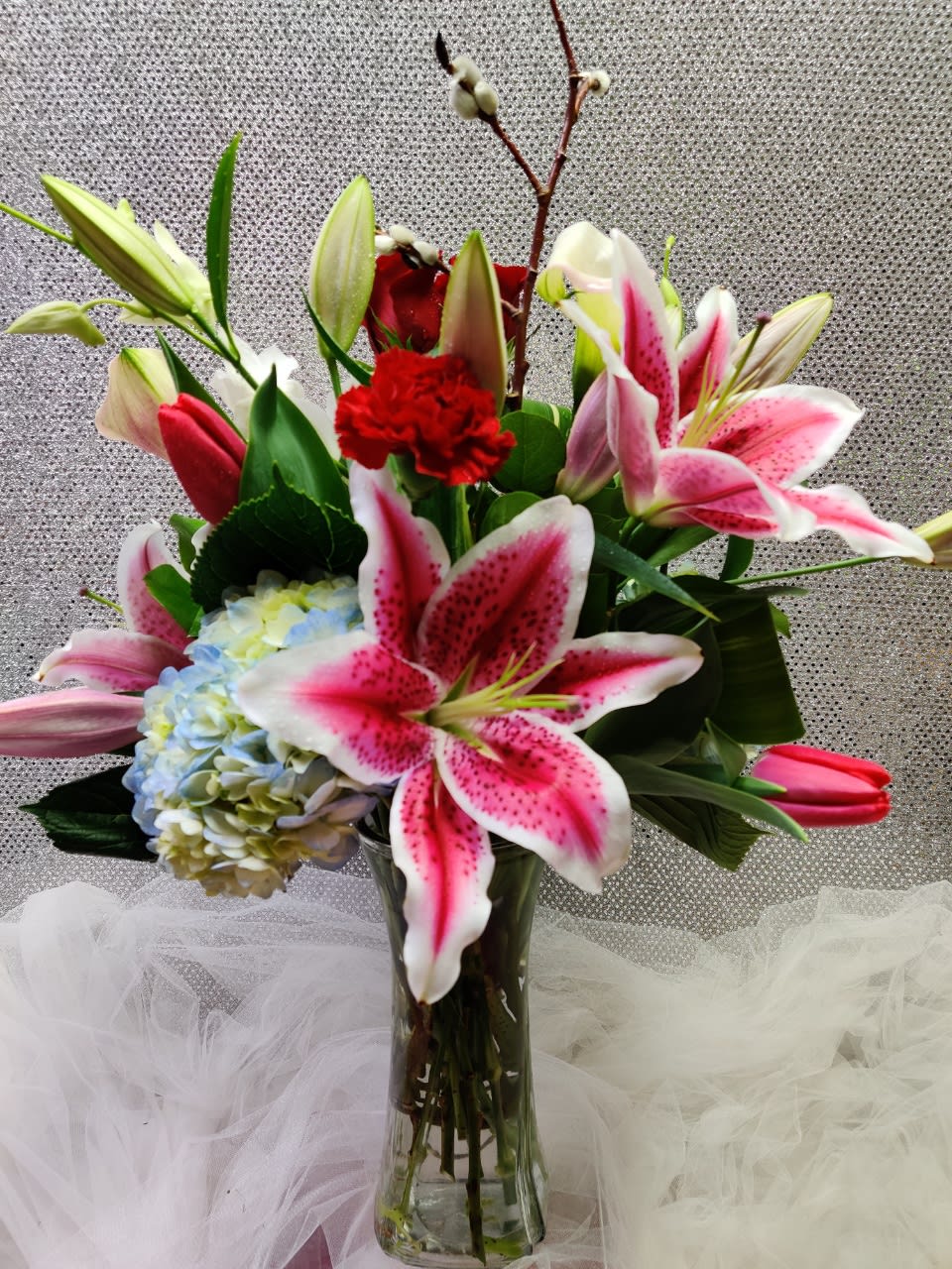 Bouquet of pink lilies, hydrangea, and red carnations in a glass vase