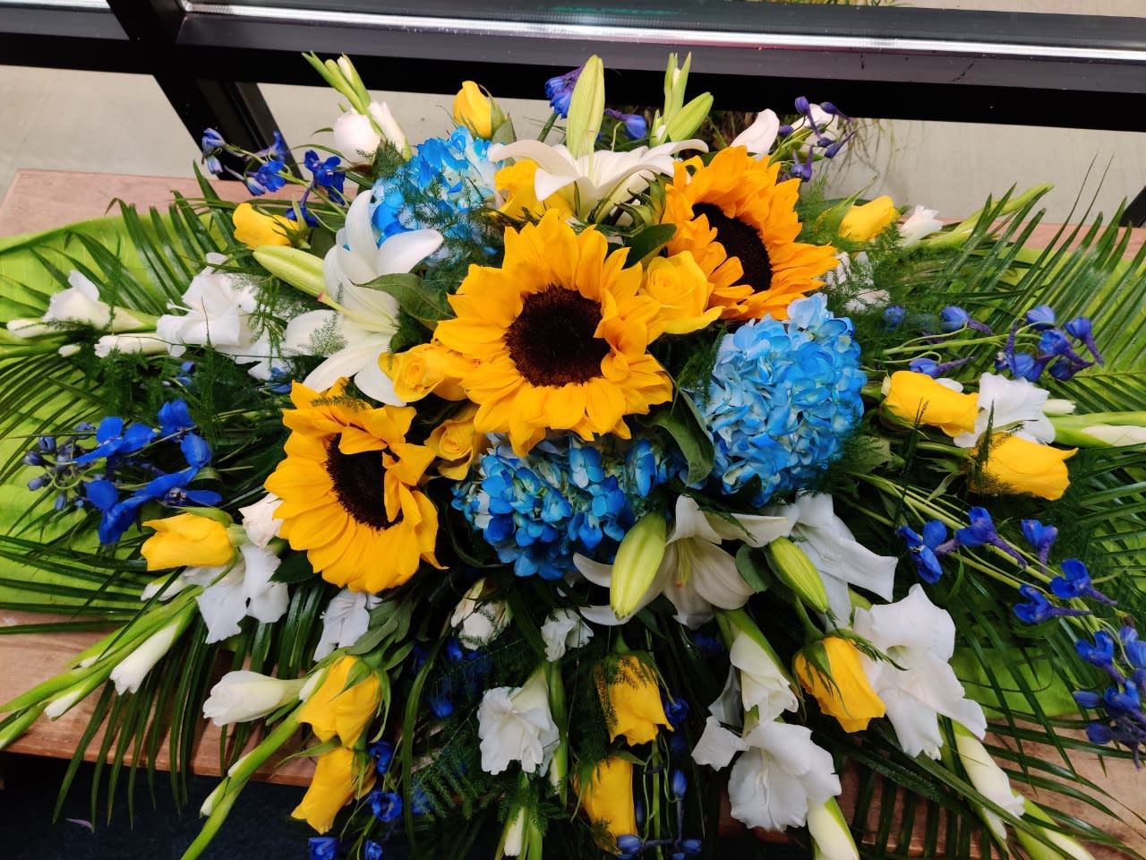 Large floral spray with sunflowers, blue hydrangeas, white lilies, and yellow roses
