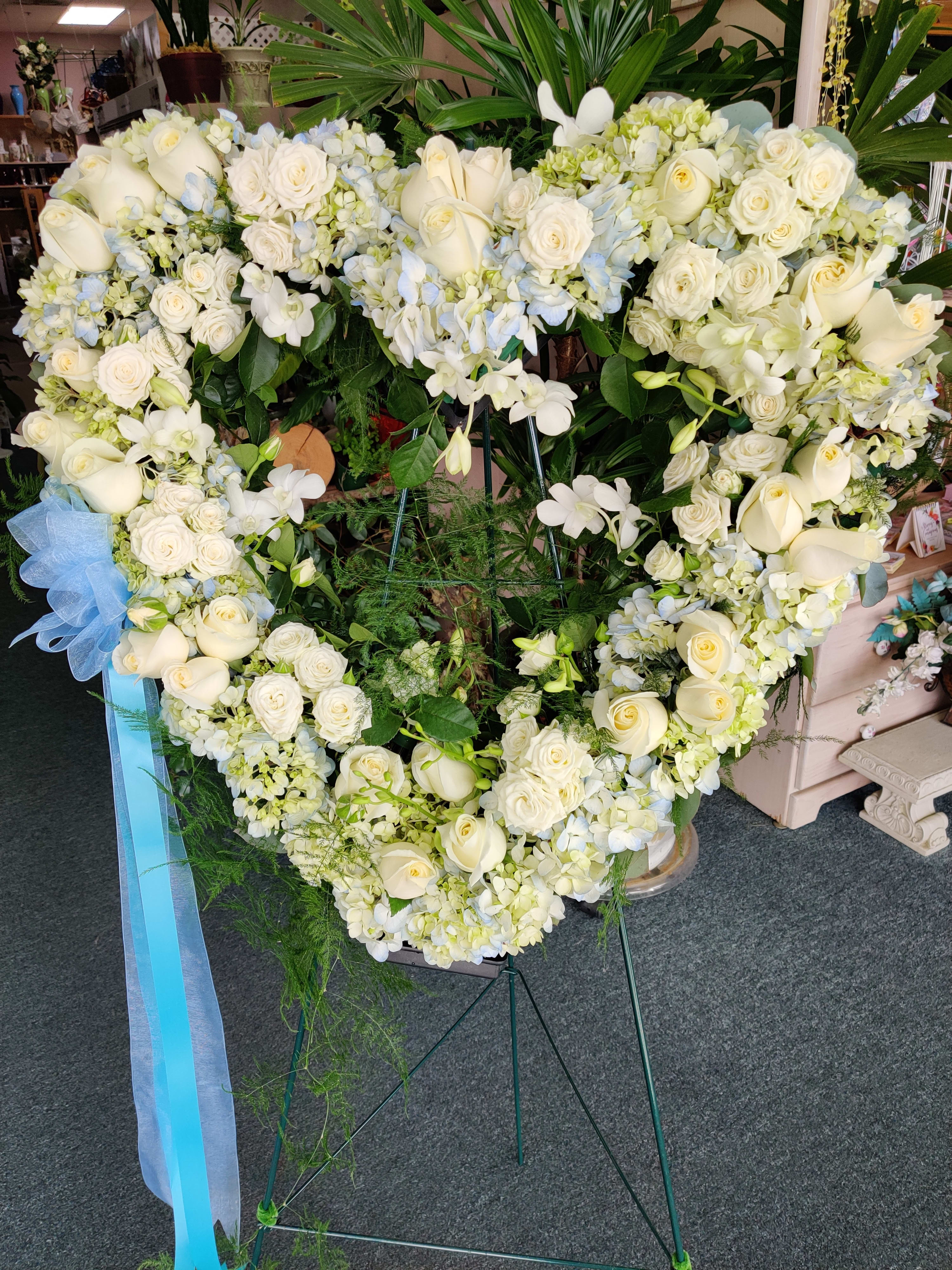 Heart-shaped white floral wreath on a stand with a blue ribbon