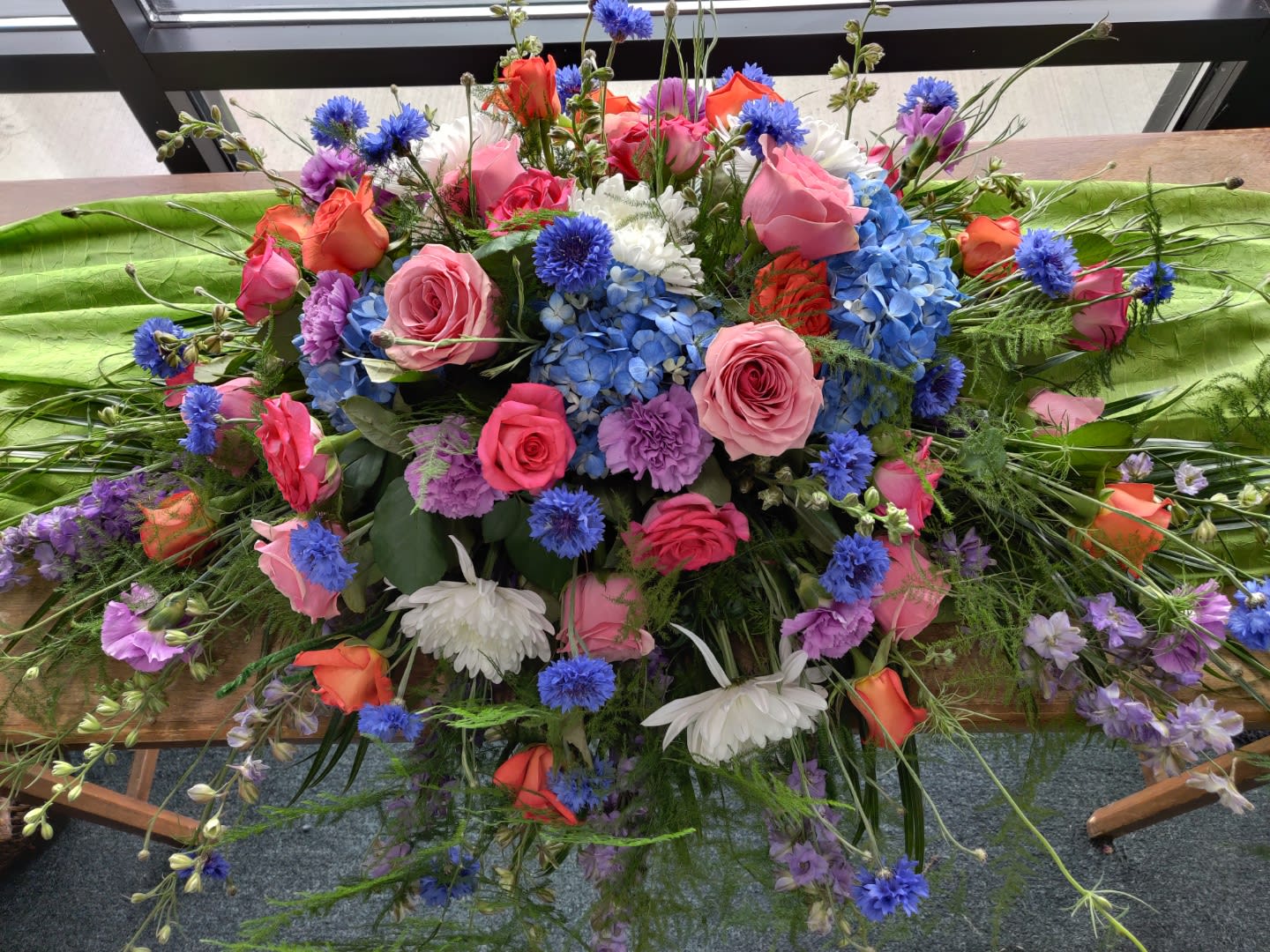 Colorful floral casket spray with roses, hydrangeas, and daisies