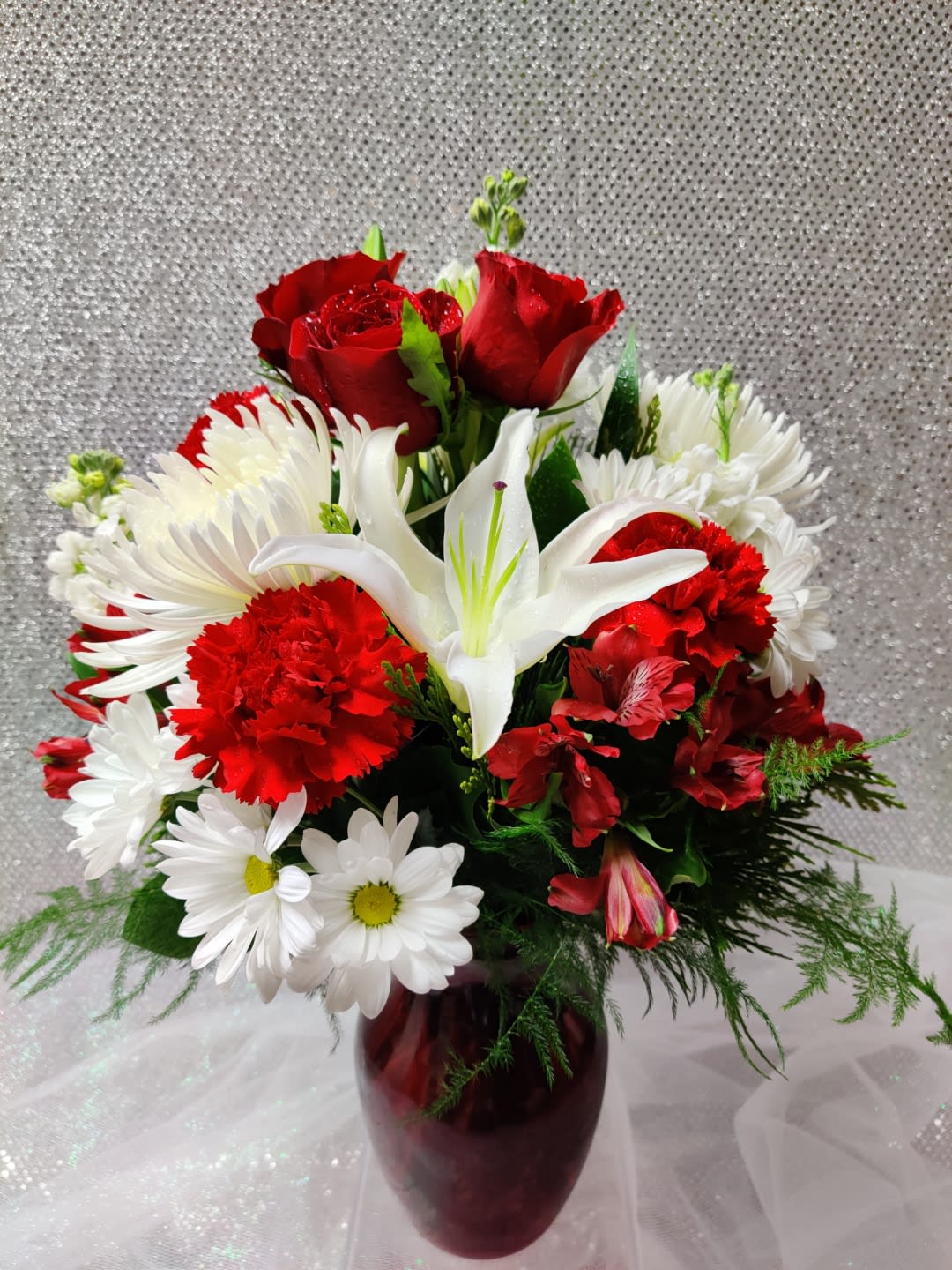 Red roses, white lilies, and daisies in a burgundy vase