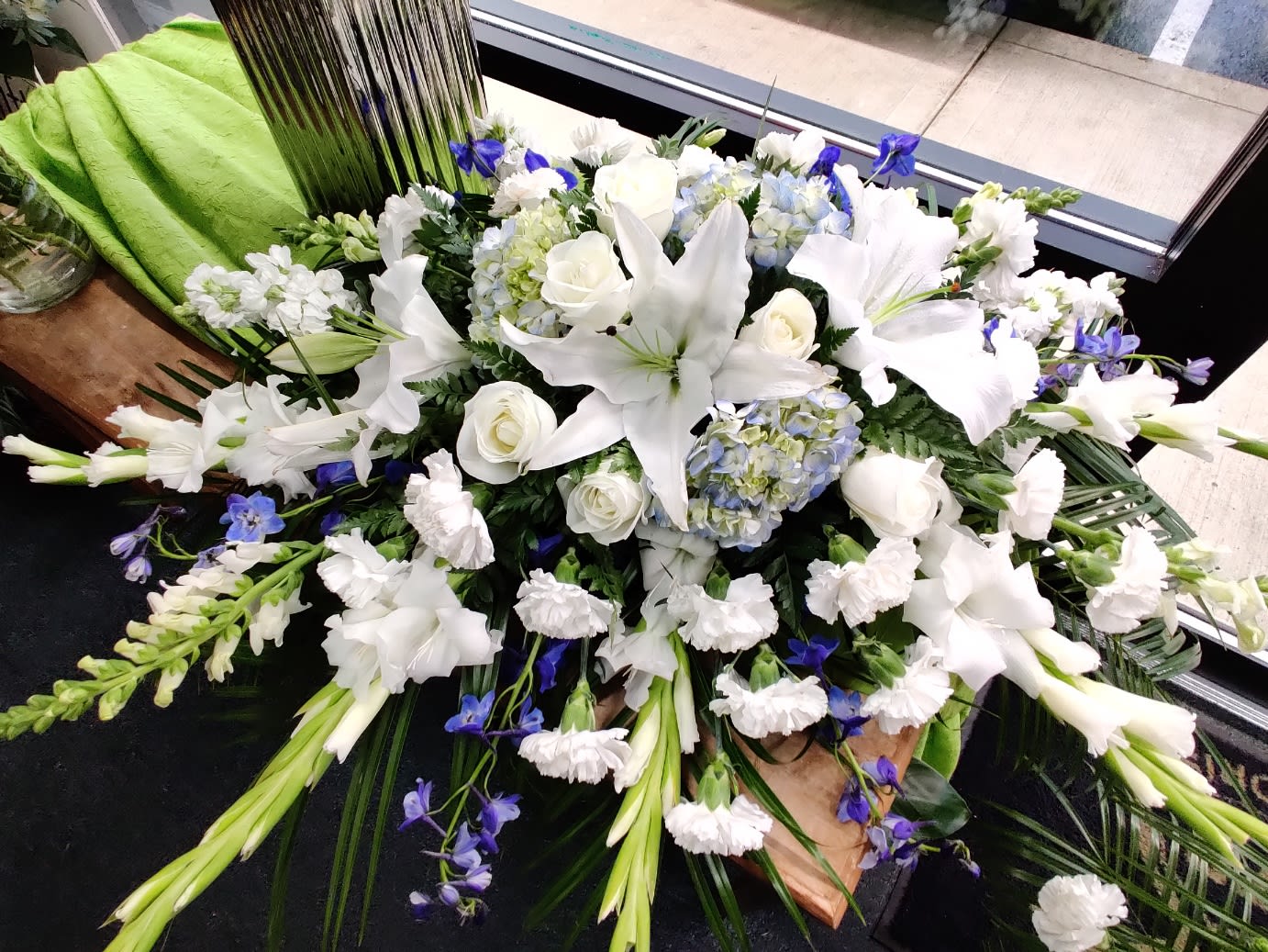 White lilies and roses with blue accents in a large casket spray