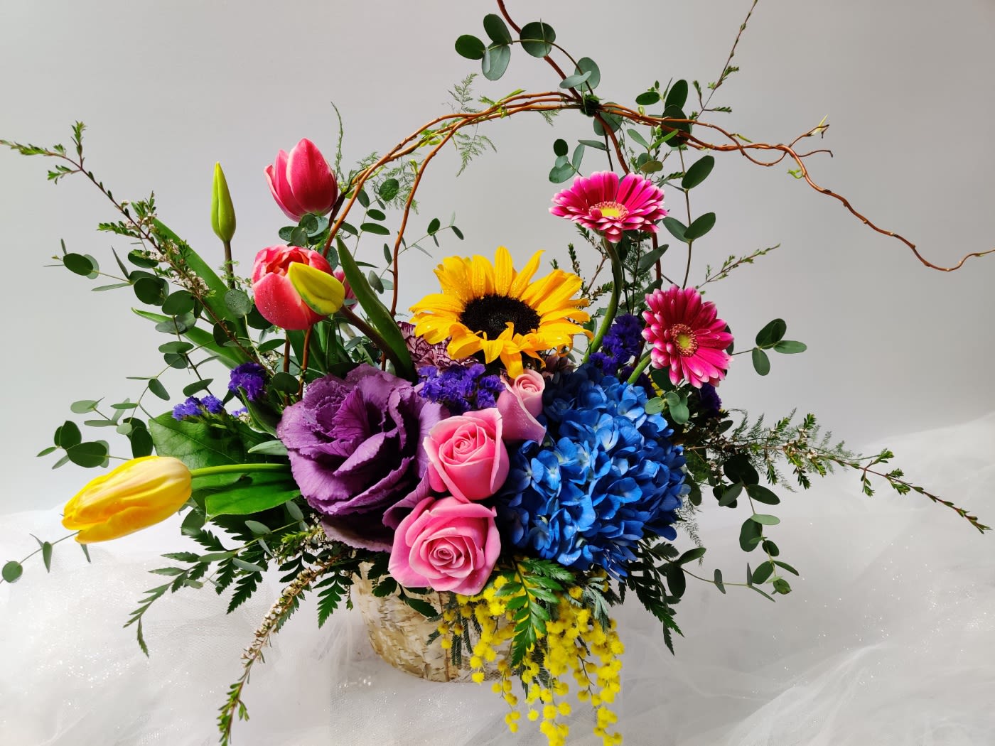 Colorful mixed bouquet with tulips, roses, sunflower, and hydrangea in a basket