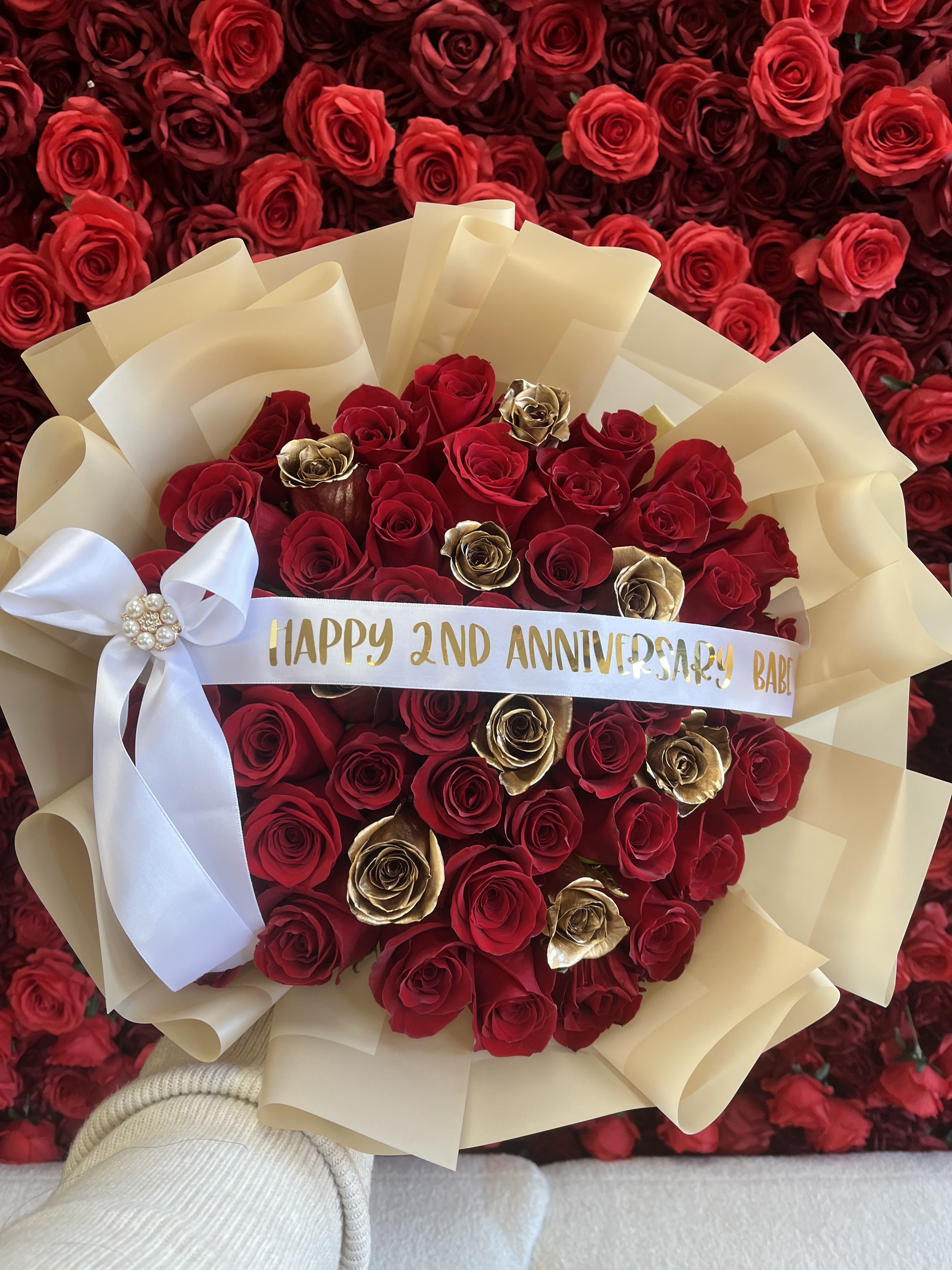 Round bouquet of red and gold roses wrapped in cream paper with a white bow and printed anniversary ribbon