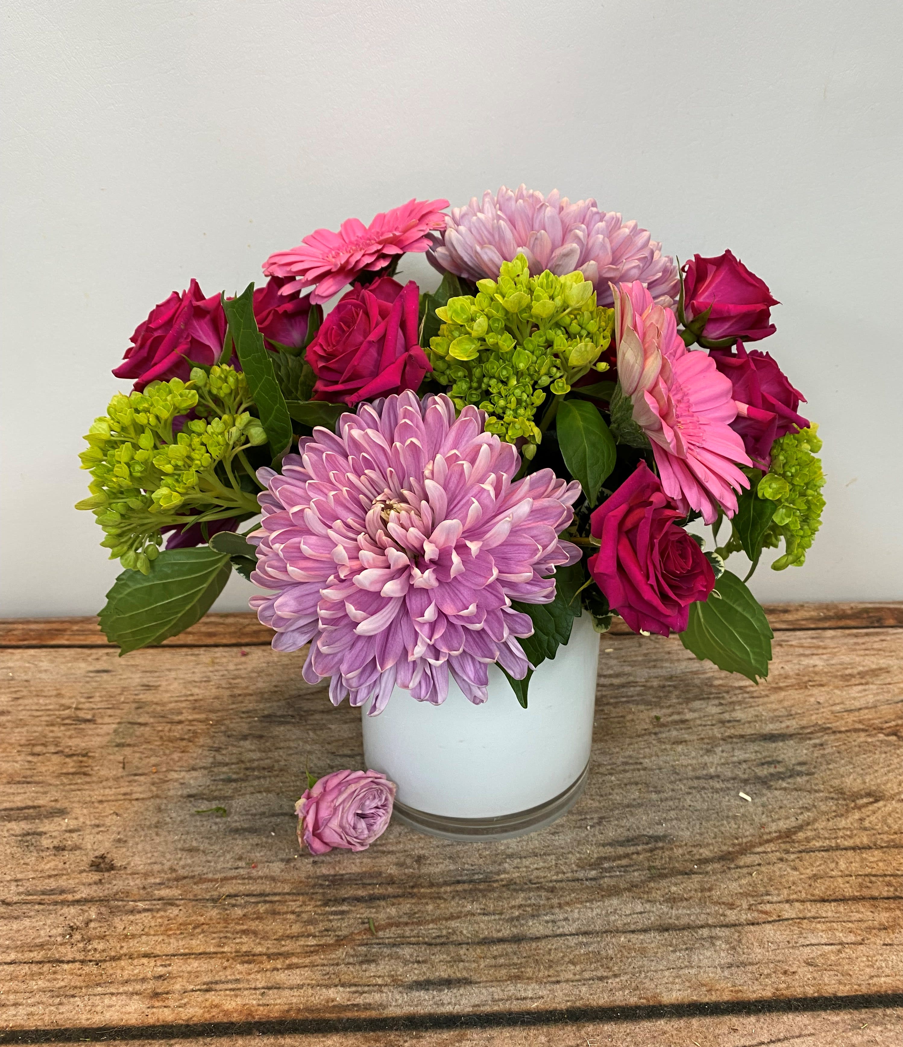 Pink roses, gerbera daisies, and lavender mum in a white vase on a wooden surface