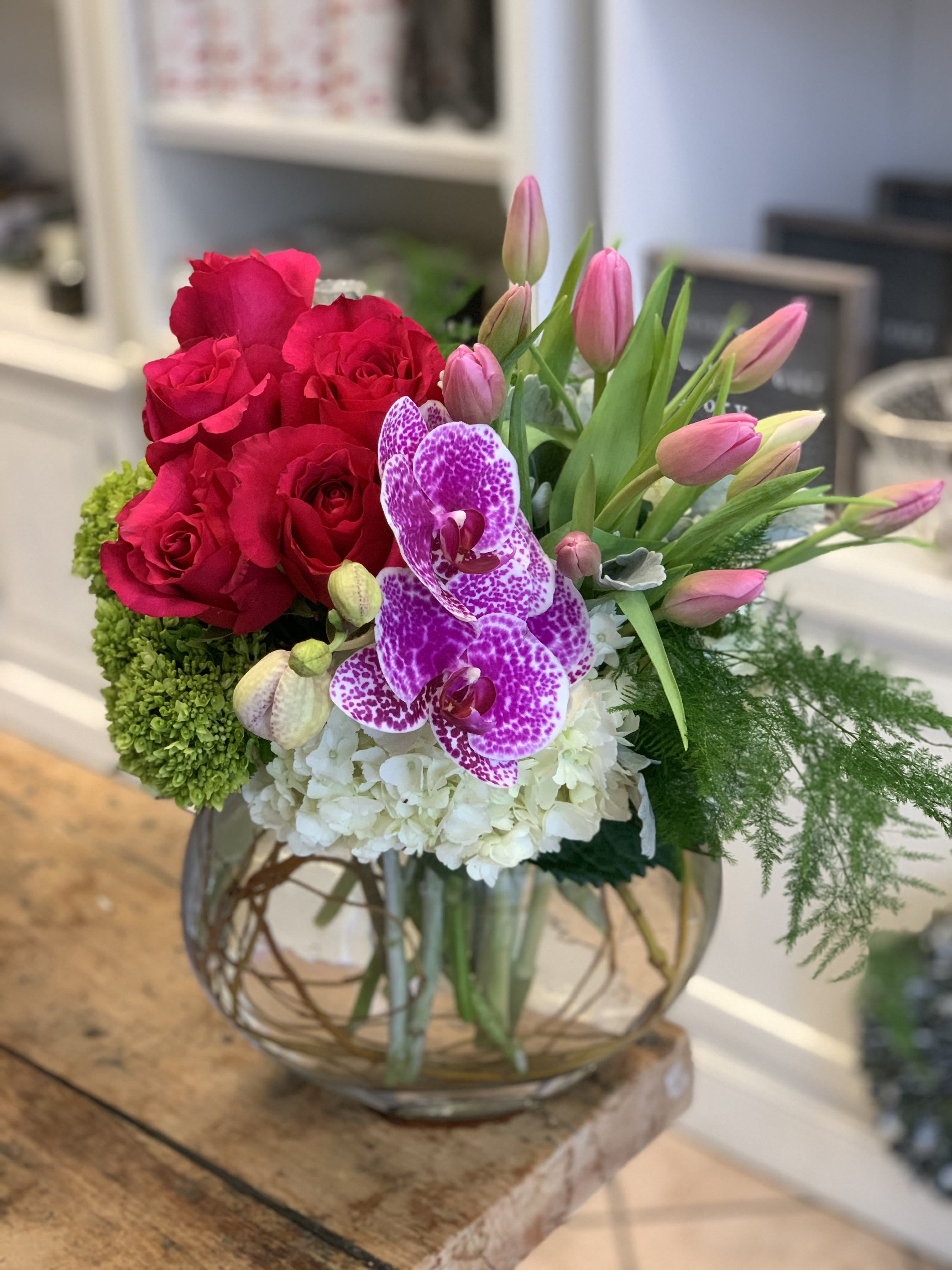 Bright pink roses, tulips and speckled orchids with white blooms in a round glass vase