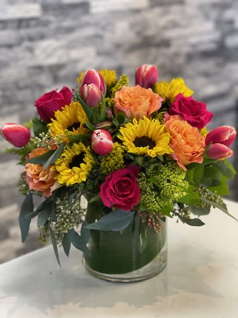 Mixed bouquet in a glass vase with roses, sunflowers, tulips, and carnations