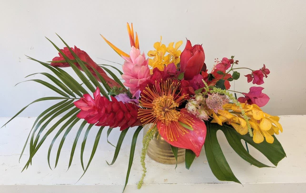 Tropical bouquet with red, pink, and yellow flowers in a gold vase