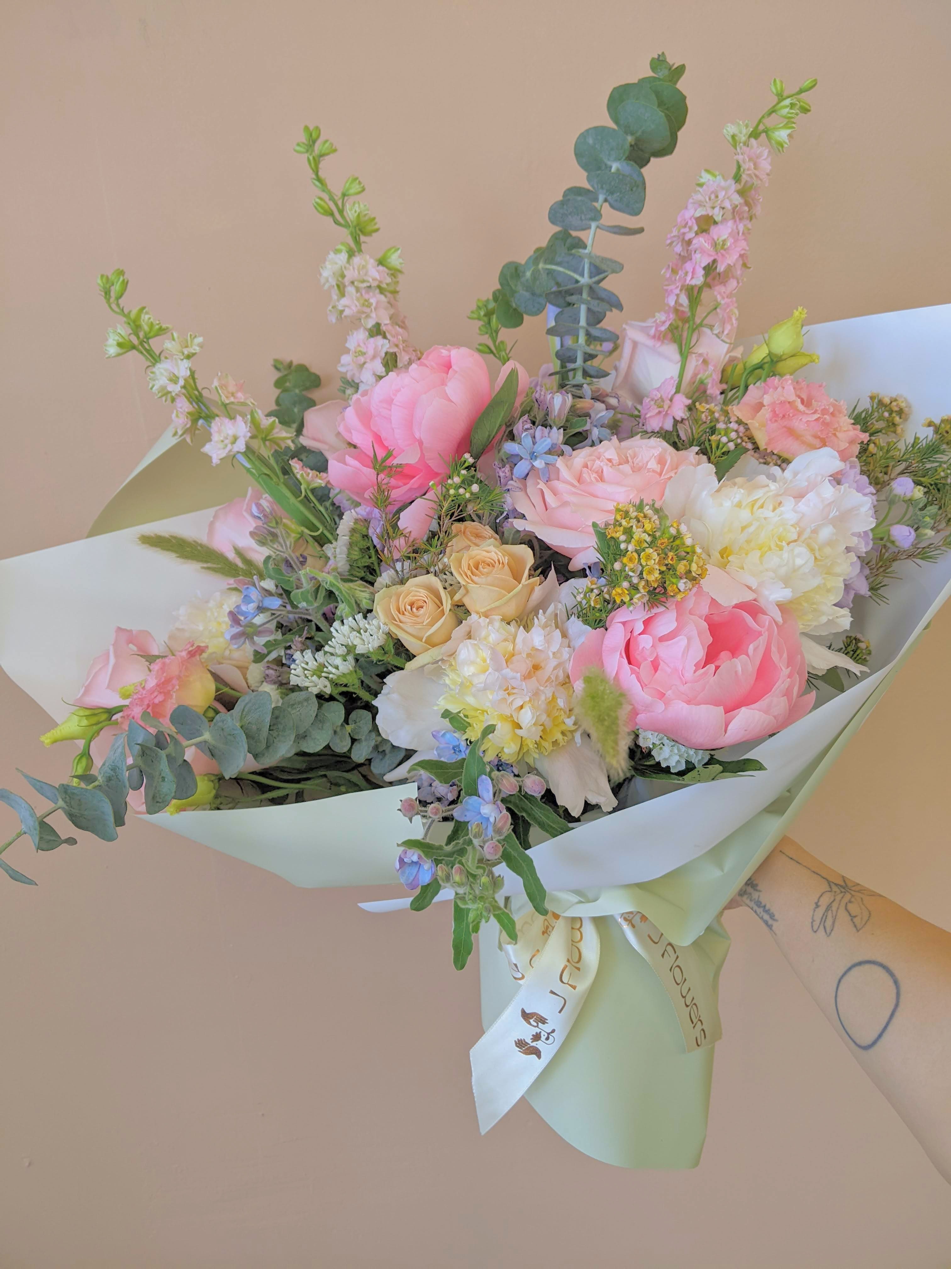 Pastel bouquet of pink, peach, and white flowers wrapped in pale paper