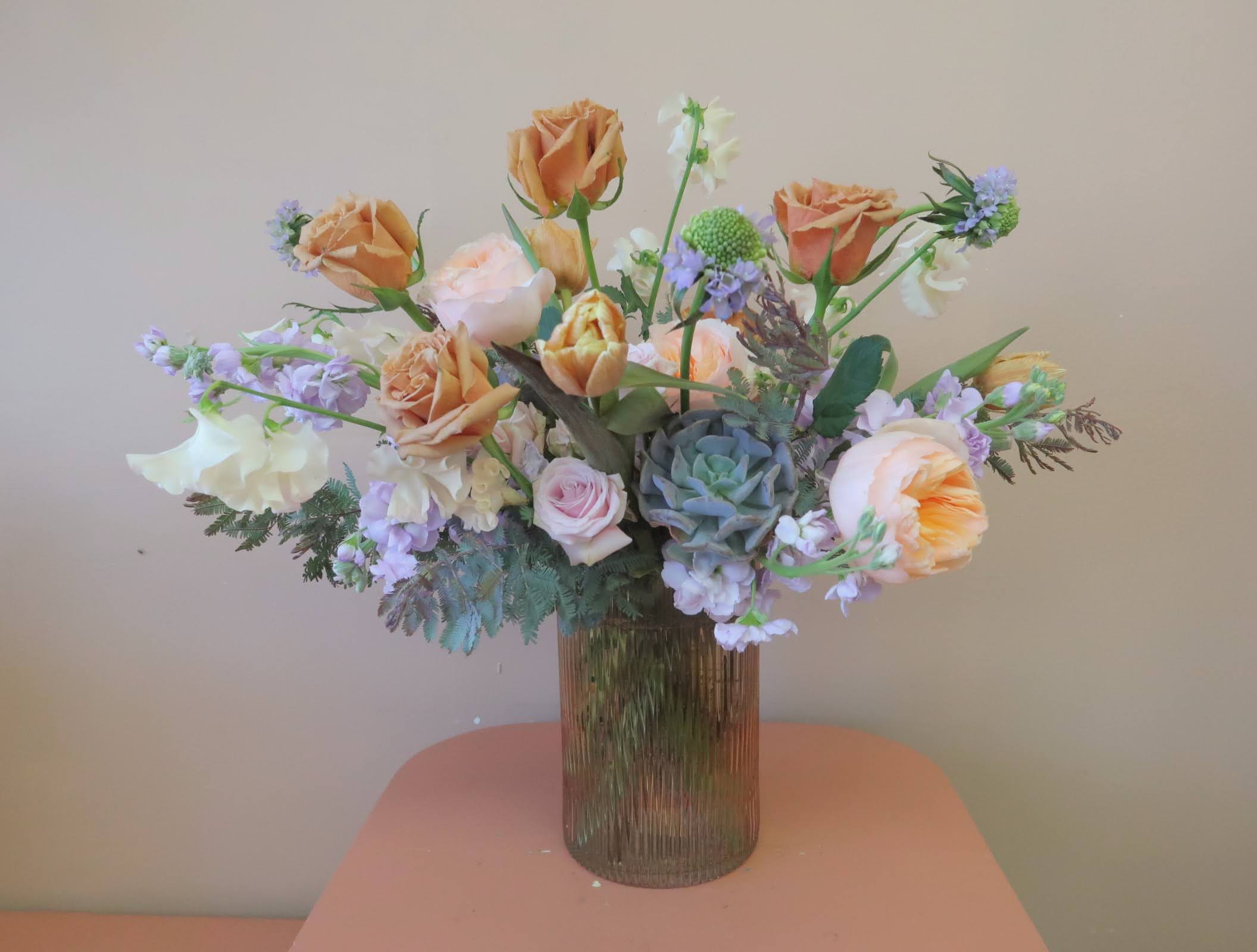 Peach roses and lavender flowers in a ribbed glass vase