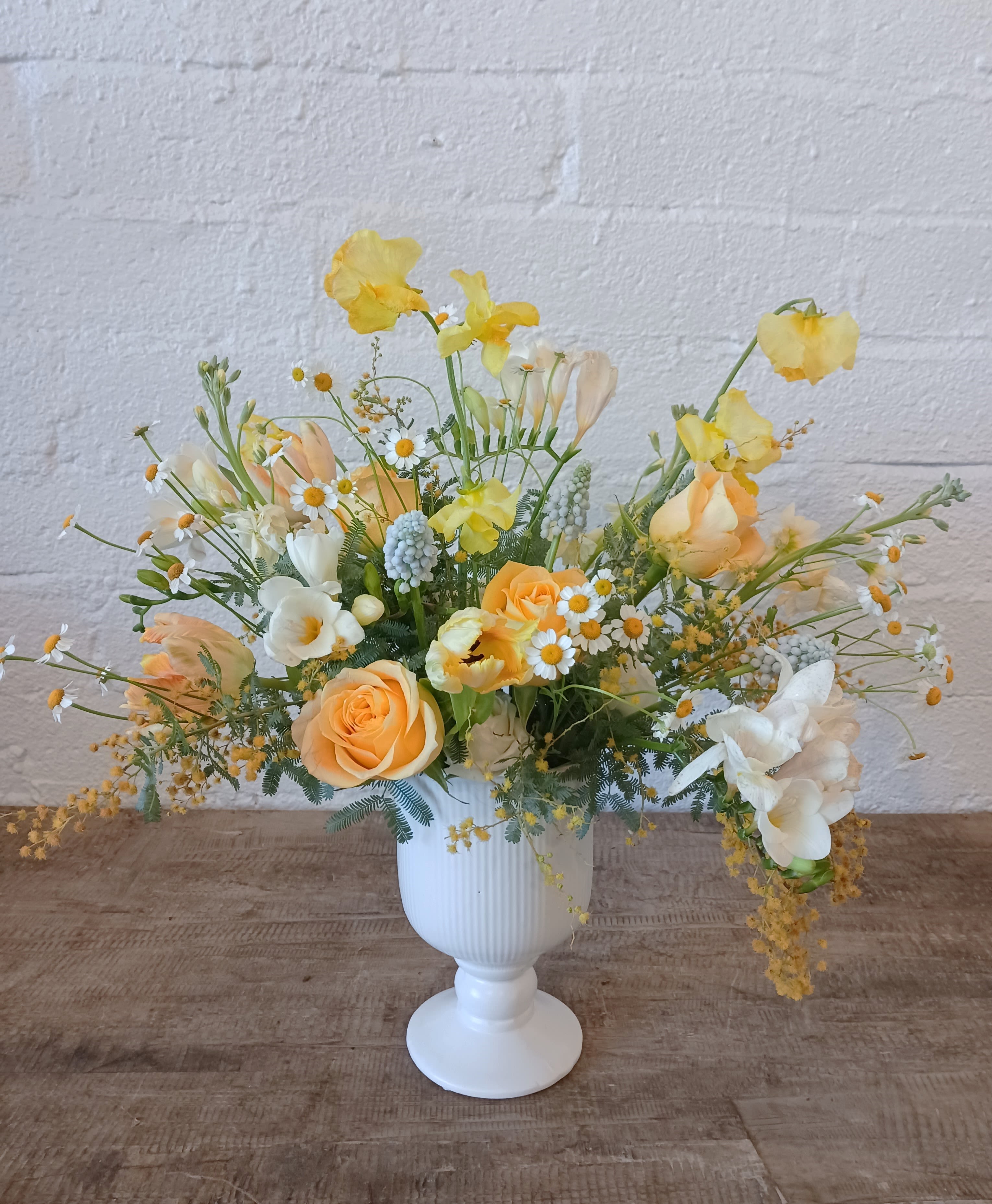 Yellow and peach floral arrangement in a white pedestal vase