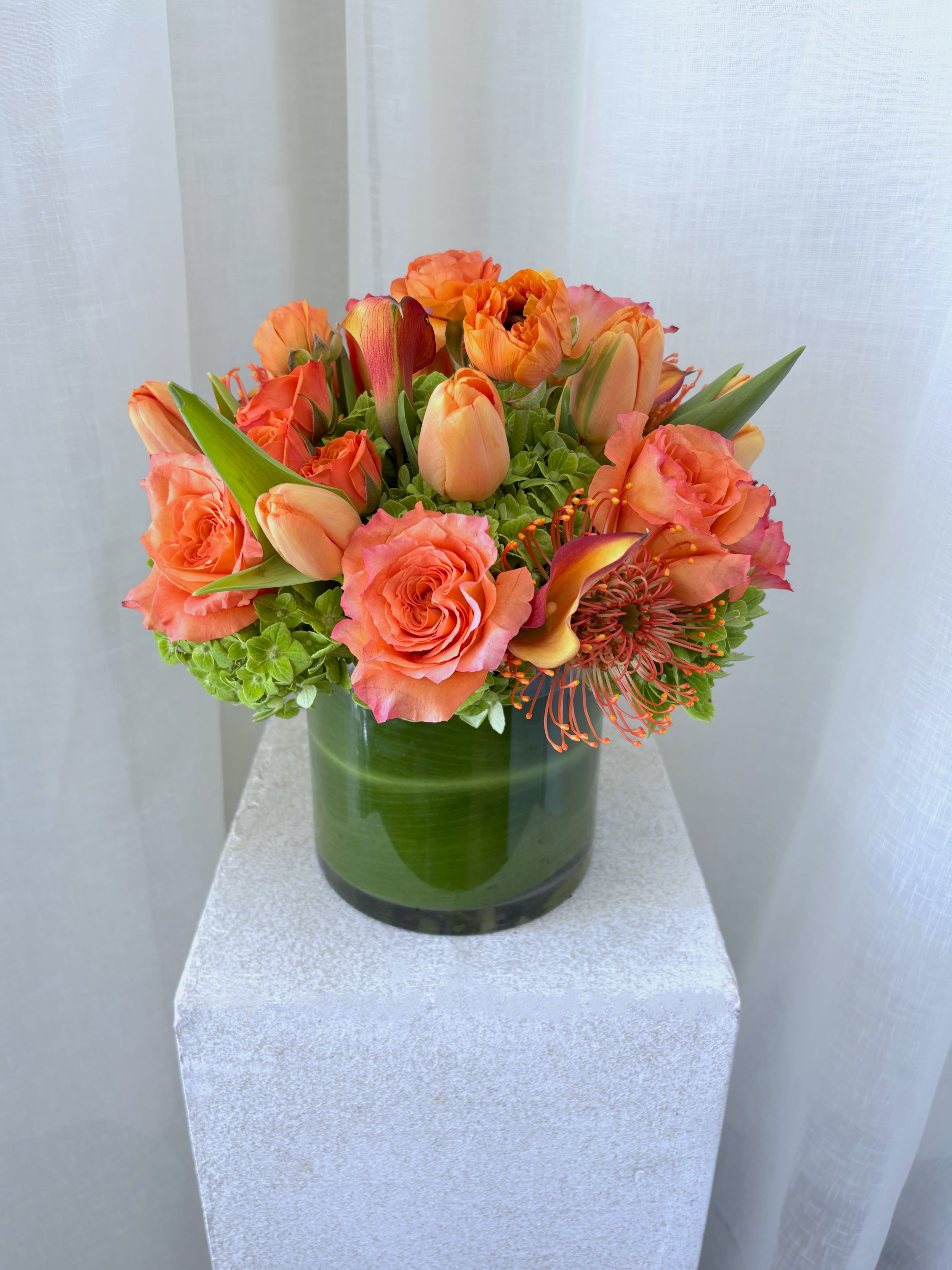 Orange roses and tulips arranged in a green glass vase