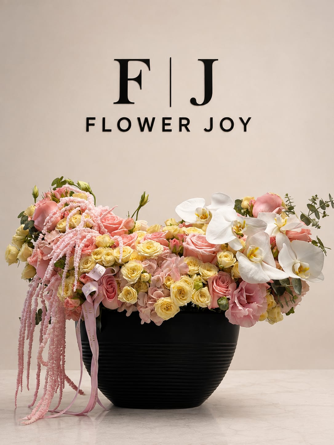 Pink and yellow floral arrangement in a black vase with white orchids